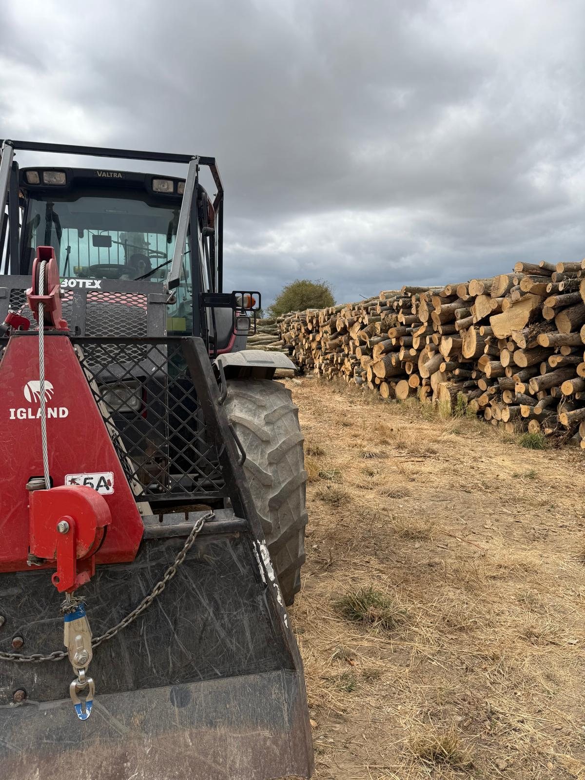 Valtra tractor and red Igland equipment beside timber stacks